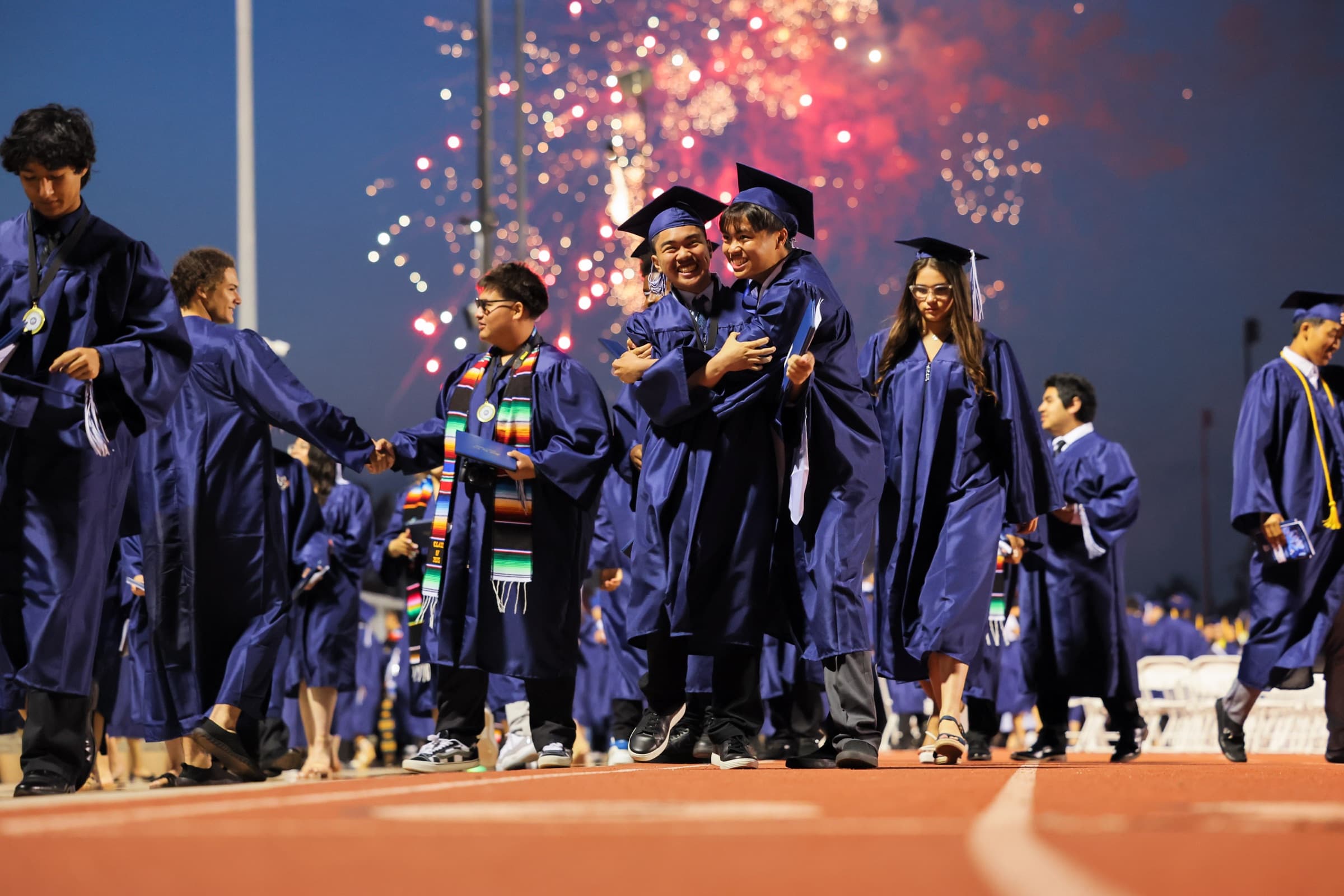 Bellflower Unified graduates celebrate on the field as fireworks light the sky